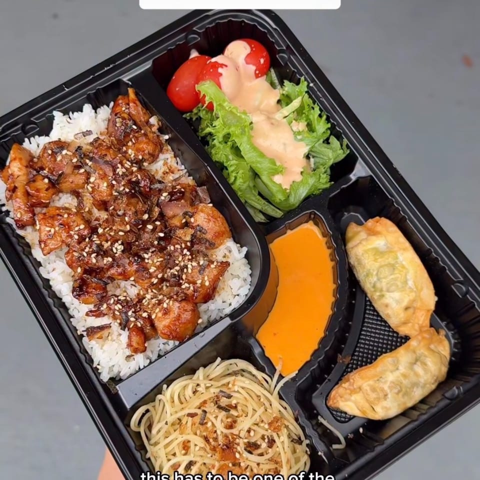 Japanese bento box with chicken, rice, salad, dumplings, noodles, and dipping sauce.
