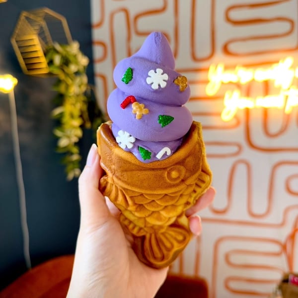Hand holding purple soft-serve ice cream in a fish-shaped waffle cone with holiday sprinkles.