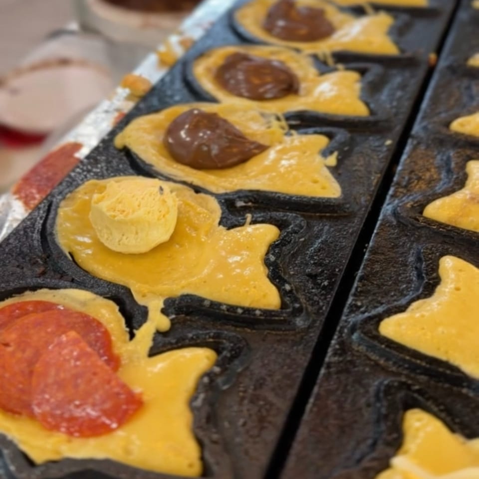 Fish-shaped taiyaki batter cooking in a mold with chocolate, pepperoni, and cheese fillings.