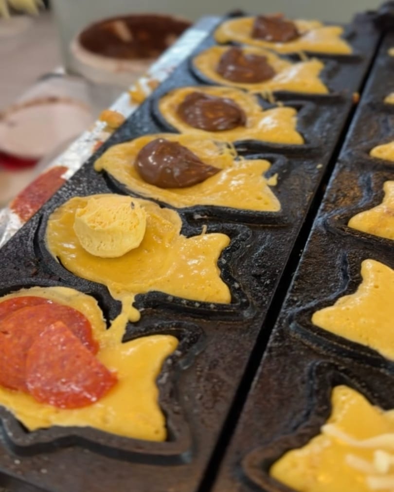 Fish-shaped taiyaki batter cooking in a mold with chocolate, pepperoni, and cheese fillings.