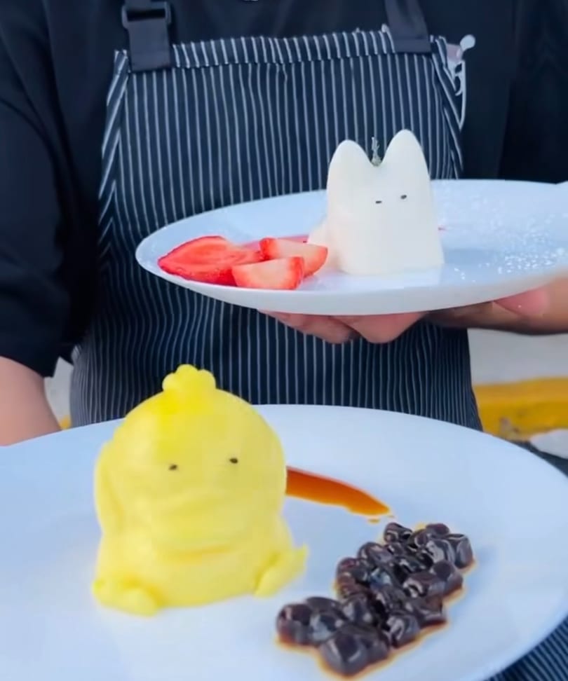 Chef holding two plates of whimsical desserts: a yellow character with boba and a white cat with strawberries.