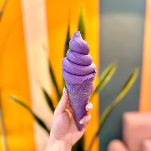 Vibrant purple soft-serve ice cream in a matching cone held by a hand.