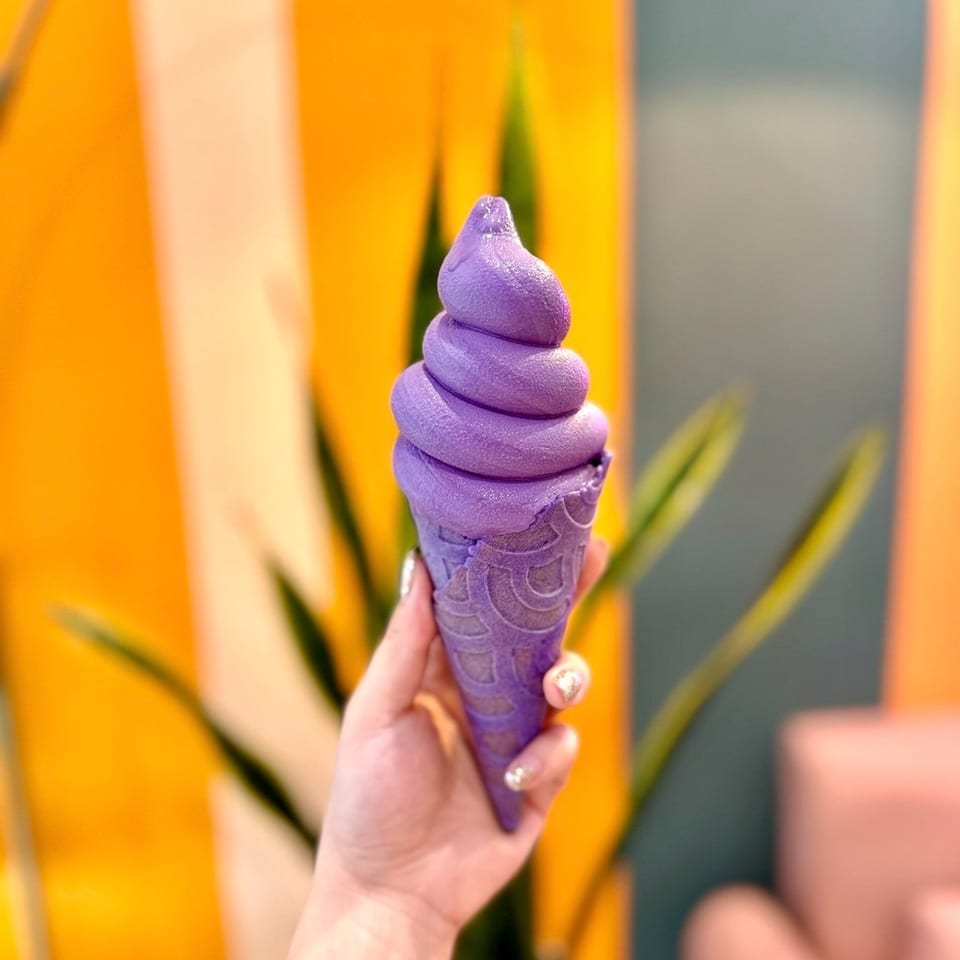 Vibrant purple soft-serve ice cream in a matching cone held by a hand.