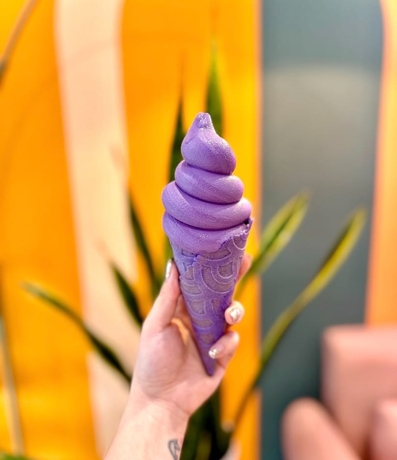Vibrant purple soft-serve ice cream in a matching cone held by a hand.