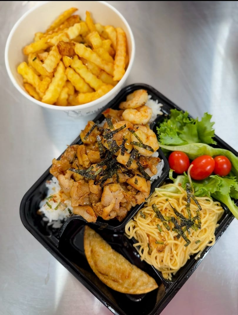 Takeout bento box with chicken, shrimp, noodles, salad, dumpling, and a cup of fries.
