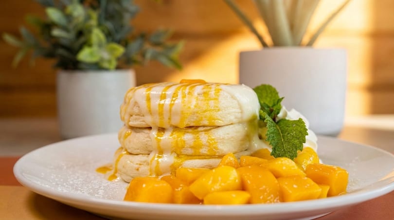 Stack of biscuits topped with mango glaze, whipped cream, mint, and diced mangoes.